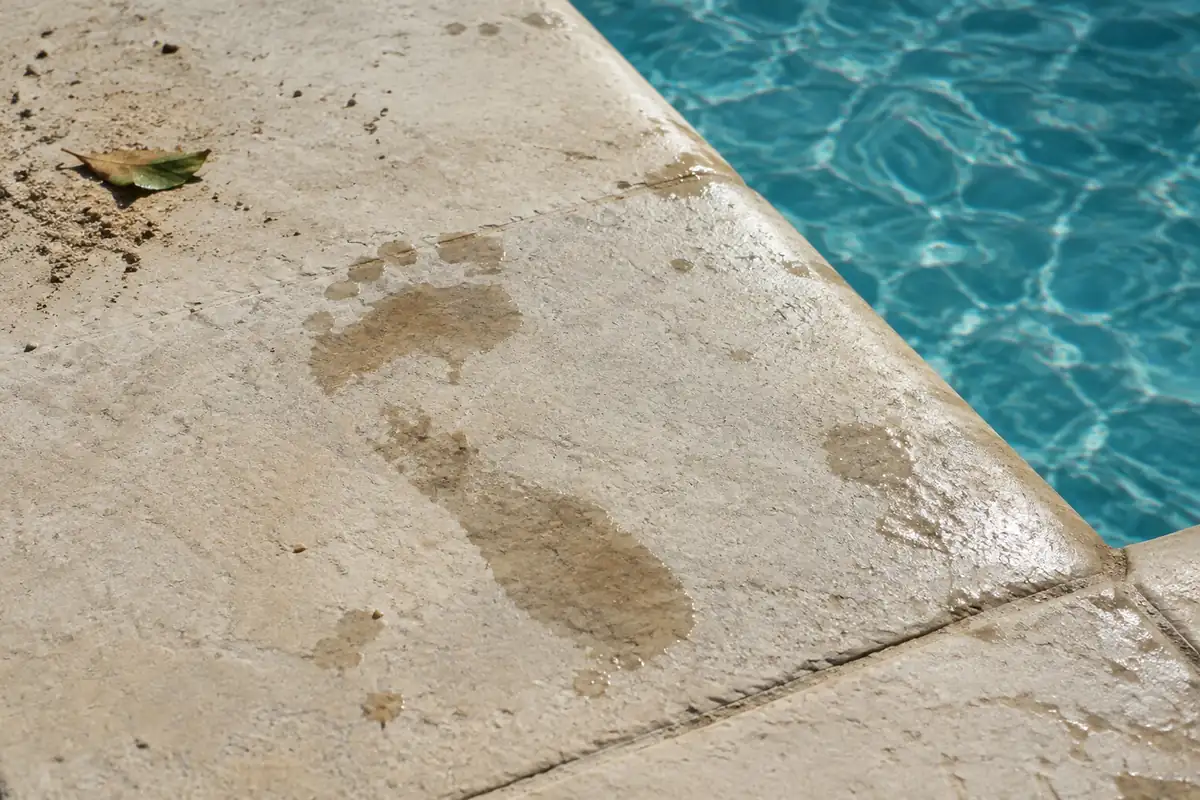 Dalles de pierre claire mouillées au bord d'une piscine, avec une trace de pied nu
